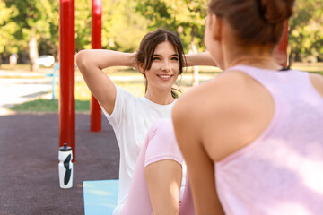 Sporty young woman doing abs exercise with her sister on sport ground