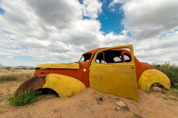 A horizontal shot of a colourful red and yellow abandoned vintage car wreck on a stormy cloudy...