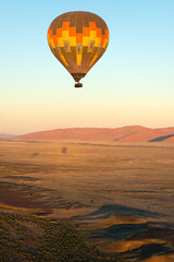 Fototapeta na wymiar A vertical shot of a hot air balloon flying over the Sossusvlei landscape at sunrise, Namibia