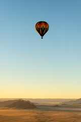Fototapeta na wymiar A vertical shot of a hot air balloon flying against a deep blue sky over the Sossusvlei landscape at sunrise, Namibia