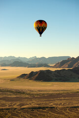 A vertical shot of a hot air balloon flying over the mountains in the Sossusvlei National Park landscape at sunrise, Namibia
