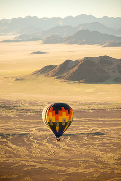 A vertical landscape shot of a hot air balloon flight over the vast Sossusvlei National Park landscape at sunrise, Namibia