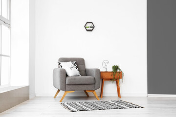 Stylish interior with bedside table and armchair on light wall background