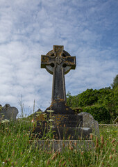 Fototapeta na wymiar Celtic cross gravestone in the grass with blue background and some clouds