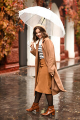 Young happy woman with umbrella walking on rainy autumn day
