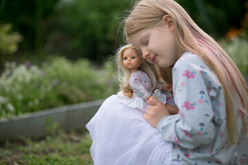 a girl walks in the garden with her favorite doll playing