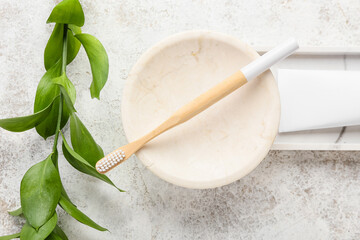 Bowl with bamboo toothbrush and plant branch on grunge background