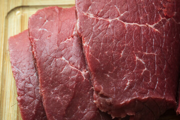 sliced raw roast beef meat on wooden cutting board closeup