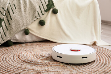 Modern robot vacuum cleaner near bed in room