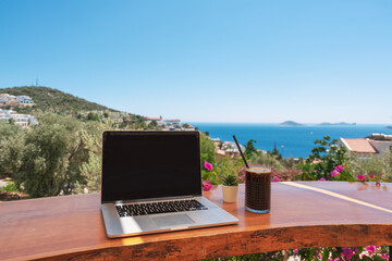 Open laptop with black screen on wooden table work space outdoors with amazing view on the ocean. Laptop on sea view backdrop. Working with view. Home office. Work remote