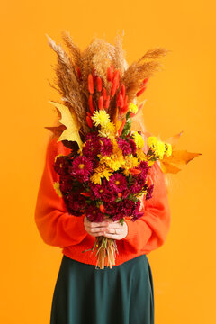 Woman covering face with beautiful autumn bouquet on color background