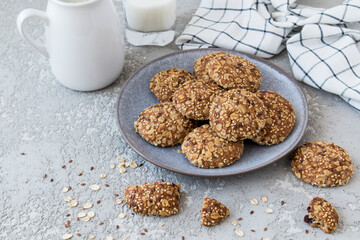 dark ceramic plate with homemade oatmeal cookies on a gray background with a jug of milk. healthy dietary food.