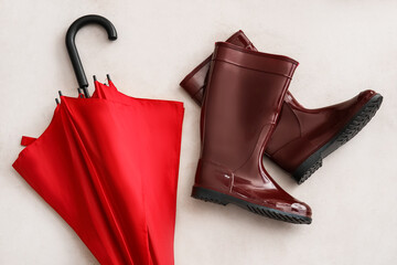 Red umbrella and rubber boots on light background