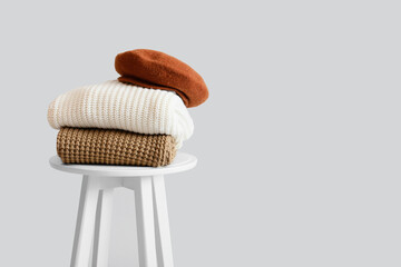 Fototapeta na wymiar Stylish winter clothes on stool against light background