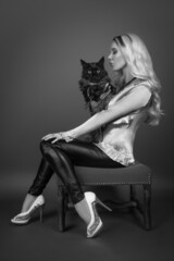 Glamorous black and white portrait of a beautiful elegantly dressed young woman pretending to kiss her black smoke purebred Maine Coon cat