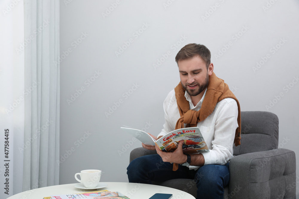 Sticker Handsome man reading magazine in armchair at home