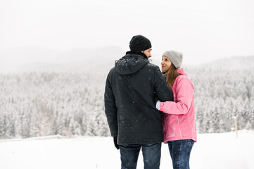 Loving couple in puffer jacket on a winter walk. Man and woman posing in the frosty forest....