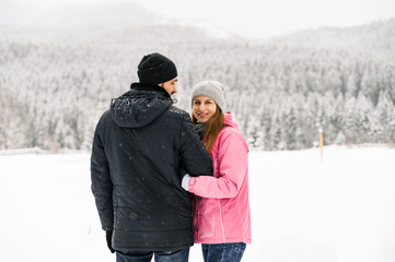 Loving couple in puffer jacket on a winter walk. Man and woman posing in the frosty forest....
