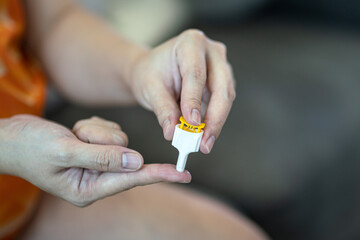 A diabetes patient is using needle device on finger for drawing blood sample to check-up sugar level. Headlthcare action with object photo. Close-up and selective focus.