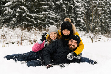 Fototapeta na wymiar Happy family have fun in winter forest and looking at camera. Mother, father and son playing with snow. Family Christmas concept. Enjoying spending time together