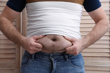 Man wearing tight t-shirt near wooden folding screen, closeup. Overweight problem