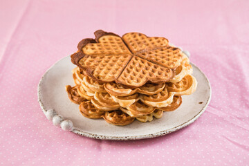 Freshly baked homemade heart shaped Belgium waffles on pink background. European baked pastry sweets. St. Valentine's Day breakfast concept.