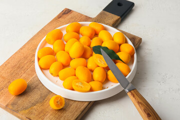 Plate with tasty kumquat fruits on light background