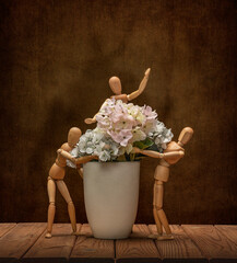 Wooden men Gestalta with a cheerful company collect flowers in a vase, on a wooden table and an artistic background.