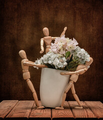 Wooden men Gestalta with a cheerful company collect flowers in a vase, on a wooden table and an artistic background.