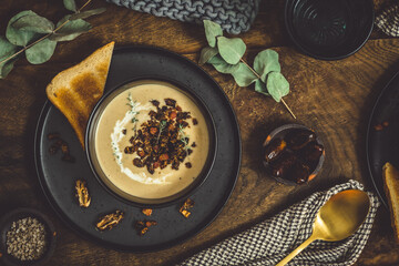 Bowl of chestnut soup with rosted topping, cream and bread in a black bowl on rustic wooden...