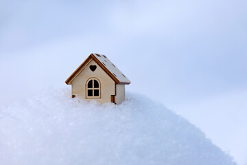 Wooden house model in a snow. Concept of country cottage, housing search in winter, real estate in ecologically clean area