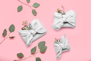 Gifts wrapped in fabric, with flowers and eucalyptus branches on pink background