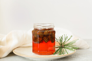 Plate with jar of tasty pine cone jam and fir tree branch on light background