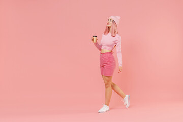Full body side view young woman with bright dyed rose hair in rosy top shirt hat hold takeaway...