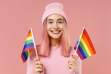 Young happy lesbian fun woman 20s with bright dyed rose hair in rosy top shirt hat hold rainbow flags isolated on plain light pastel pink background studio portrait. People lifestyle fashion concept.