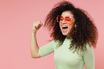 Overjoyed jubilant happy young curly latin woman 20s wear mint t-shirt sunglasses doing winner...