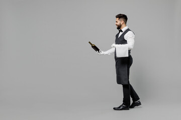 Full size young barista male waiter butler man 20s wear white shirt vest elegant uniform work at cafe give bottle of wine isolated on plain grey background studio portrait Restaurant employee concept - Powered by Adobe