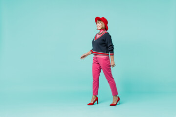 Full body smiling happy cheerful elderly caucasian woman 50s wear necklace shirt red hat walking go strolling isolated on plain pastel light blue background studio portrait. People lifestyle concept.
