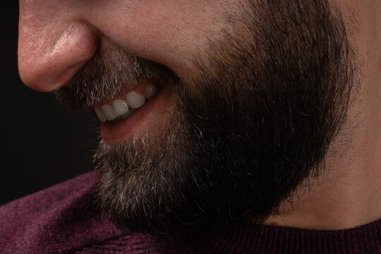 close-up portrait in profile of young smiling, happy man with thick black beard and mustache on black background.