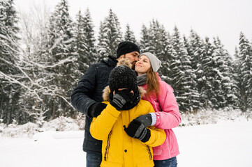 Happy family have fun in winter forest and looking at camera. Mother, father and son playing with snow. Family Christmas concept. Enjoying spending time together