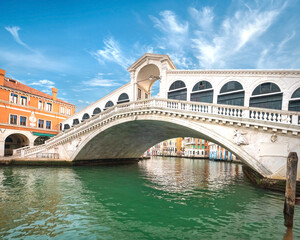 Fototapeta na wymiar Rialto bridge on The Grand Canal in Venice, Italy. Romantic architecture of Venice, famous landmark on a bright sunny day, blue sky with clouds.