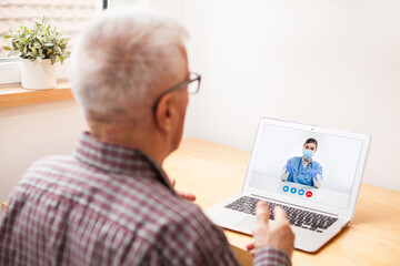 Fototapeta na wymiar Elderly senior man talking to young female doctor via laptop video call