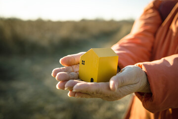 Close-up of female hand holding wooden white house model with autumn natural and sunlight background