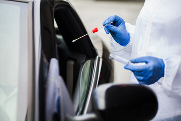Medical worker's hands in gloves holding PCR testing kit in mobile testing drive-thru center