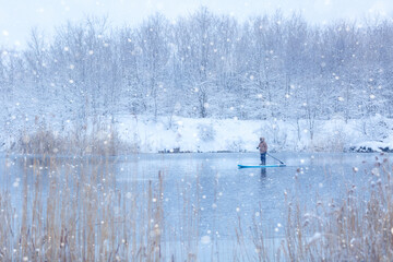 Winter SUP. Man rides on a supboard in snowfall on the river