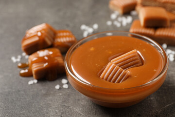 Tasty salted caramel with candies in glass bowl on grey table, closeup