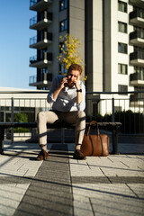 Young stylish businessman sitting on the beanch outdoors. Portrait of handsome man talking to the phone.