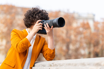 Fototapeta na wymiar Young brunette woman with curly hair taking a picture with telephoto lens