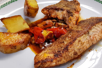 Fried Salmon fish with fresh tomato, sweet red bell pepper and olive oil with lemon. Garnish - pieces of grilled potatoes. Fish dish is served on a white plate. Healthy seafood