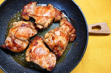 Fried chicken legs fillet served on black frying pan. Rustic wooden  board. Yellow tablecloth 